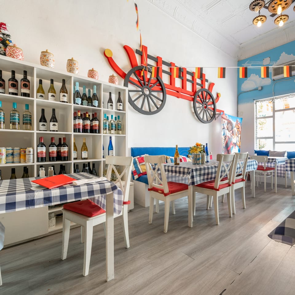 Restaurant interior with checkered tablecloths, white chairs with red cushions, and a large red wagon decoration.
