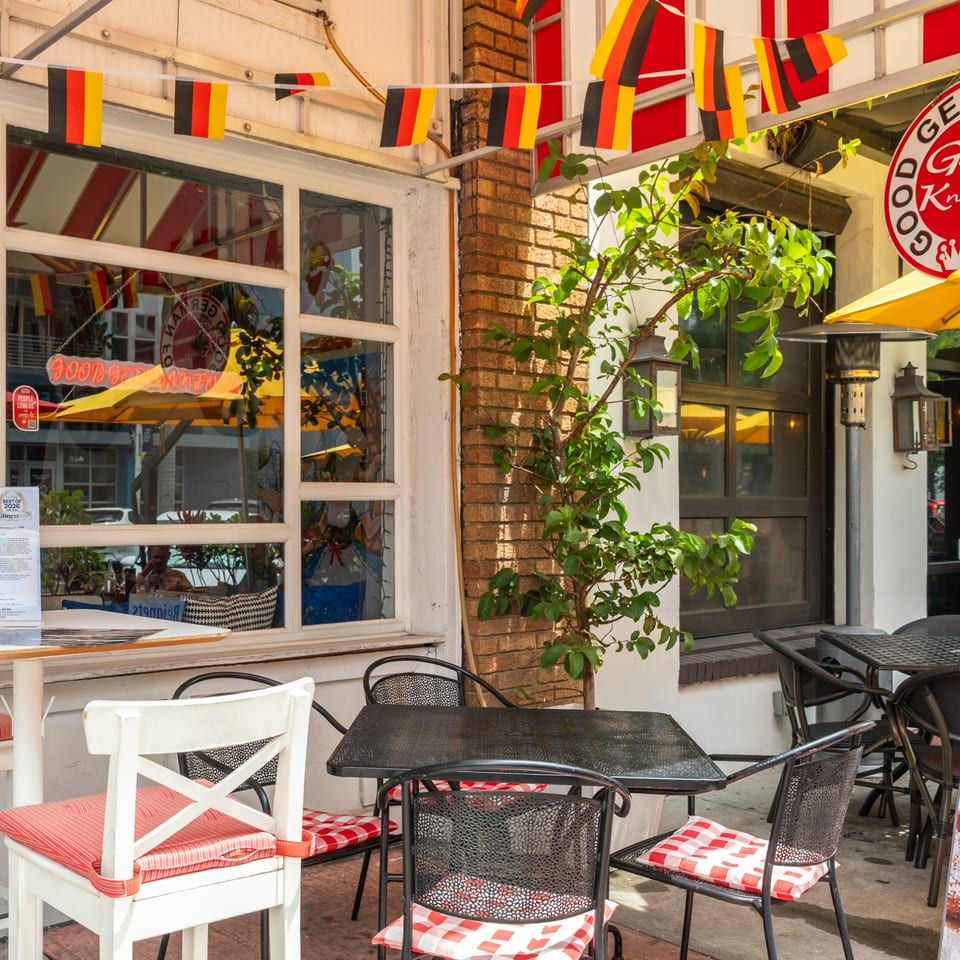 Outdoor patio of a German restaurant with black and red checkered cushions and German flag bunting.