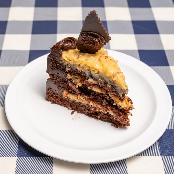 A slice of German chocolate cake with coconut-pecan frosting and chocolate ganache on a white plate.