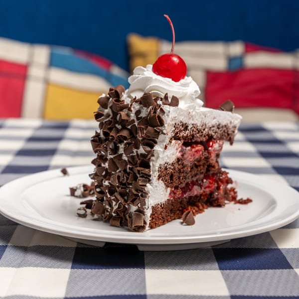 A slice of Black Forest cake with whipped cream, chocolate shavings, and a cherry on top.
