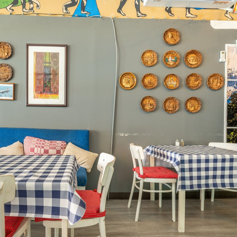 Restaurant interior with blue and white checkered tablecloths, white chairs with red cushions, and decorative wall plates.